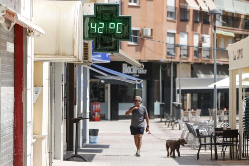 Un hombre pasea con su perro ante un termmetro urbano que marca una temperatura de 42 en la localidad valenciana de Xtiva. EFEManuel BruqueArchivo