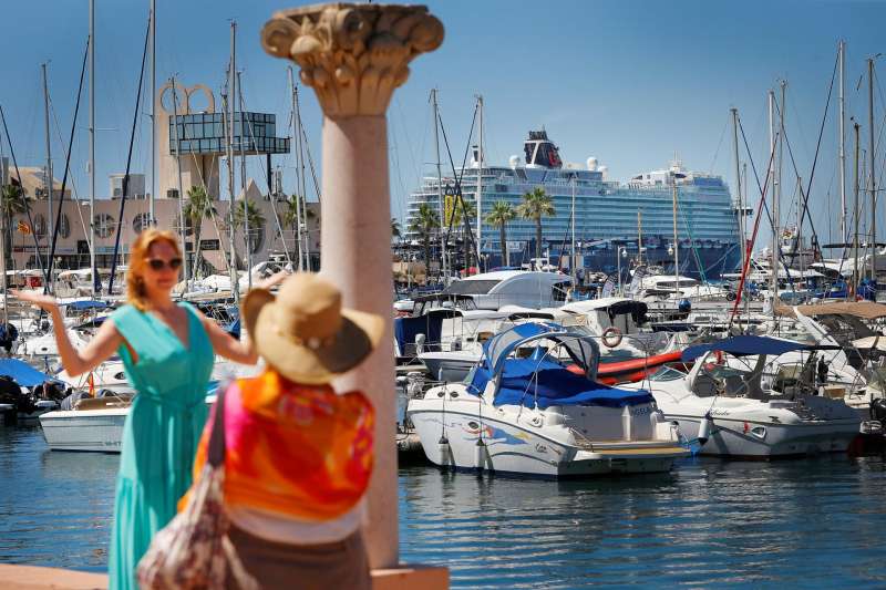 Unas turistas se toman una foto con un crucero a lo lejos, en Alicante. EFE/ Manuel Lorenzo/Archivo
