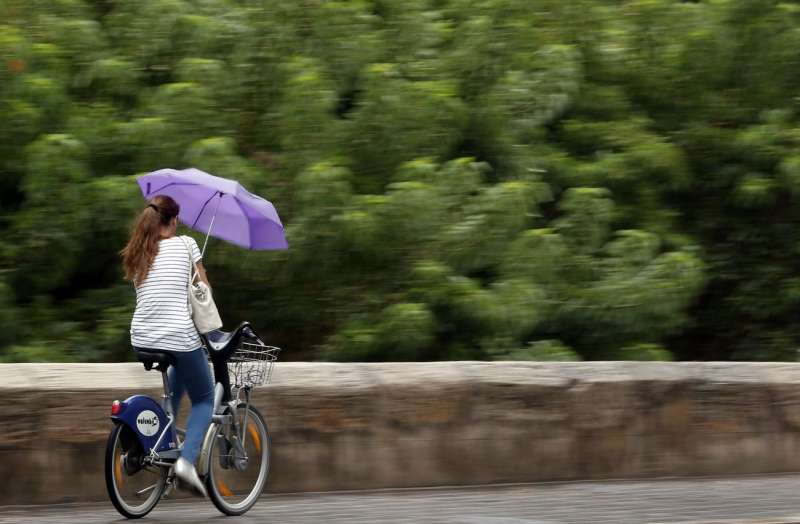 Una joven montada en una bicicleta se protege con un paraguas de la lluvia. EFE/Kai Försterling/Archivo
