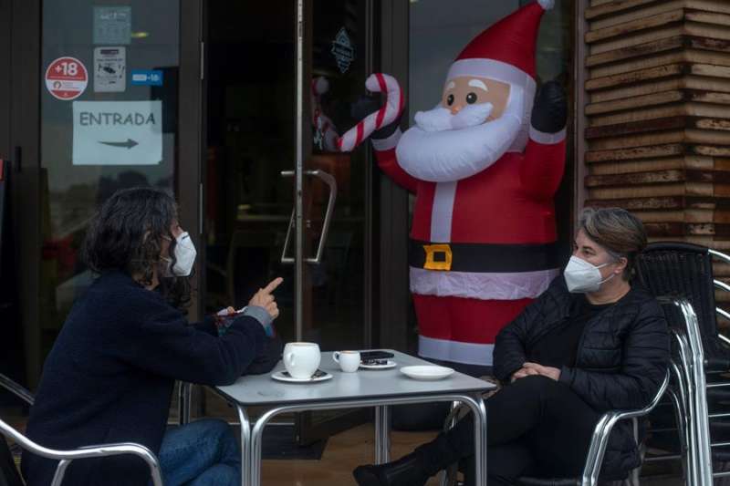 Dos personas conversan con la mascarilla puesta mientras se toman algo en la terraza de un bar en la víspera de Nochebuena. EFE/ Brais Lorenzo

