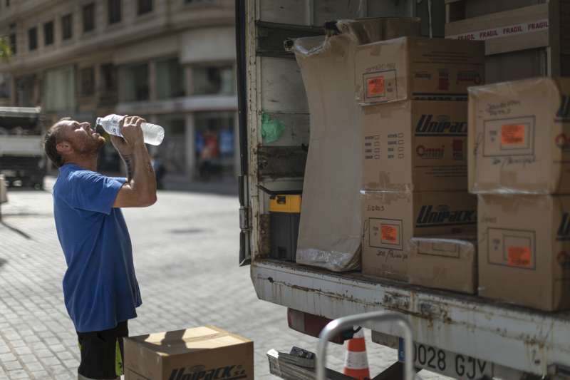 Un trabajador de una empresa de mudanzas bebe agua para combatir el calor en una calle del centro de Valencia. EFE/Biel Aliño

