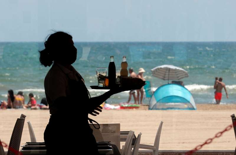 Una camarera lleva una bandeja con bebidas en un restaurante de la playa de la Malvarrosa en Valencia. /EFE