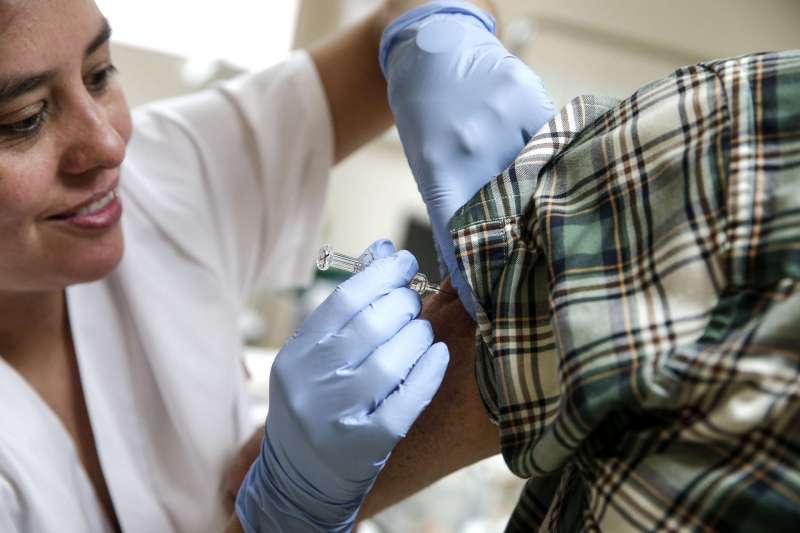 Una enfermera coloca una dosis de la vacuna de la gripe a una paciente. /EFE