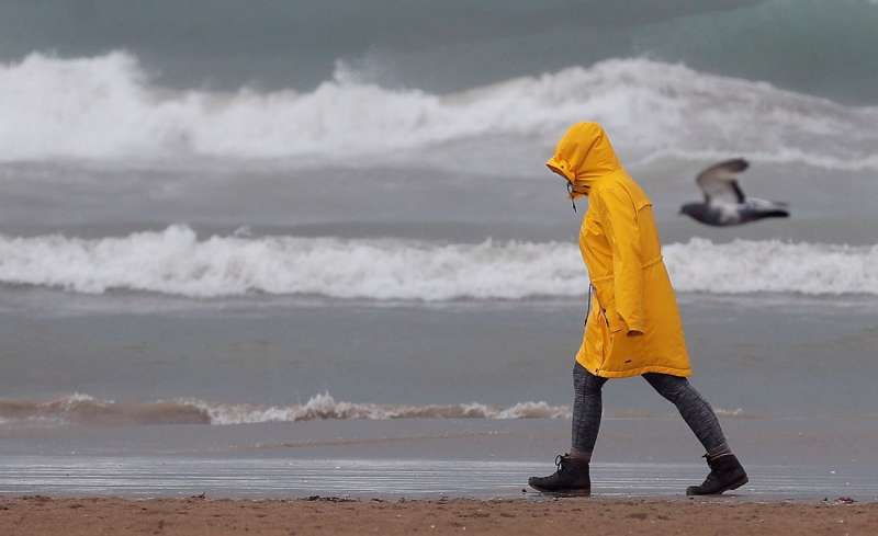 Una persona pasea por la playa de la Malvarrosa de València bien protegida contra la lluvia en un día de temporal. EFE/Kai Försterling

