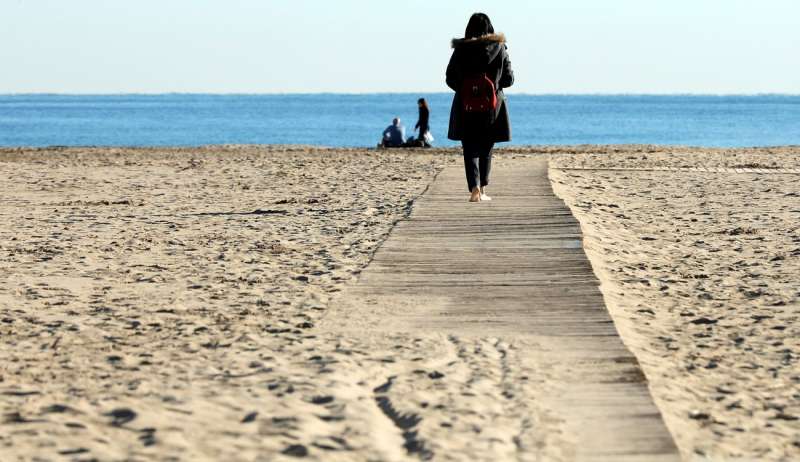 Una mujer pasea por la playa de la Malvarrosa de València en un día de invierno frío pero en el que luce el sol, con el cielo despejado. EFE/ Juan Carlos Cárdenas/Archivo

