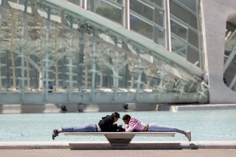 Imagen de archivo de dos personas descansando al sol sobre un banco de Ciudad de las Artes y de las Ciencias de Valencia. EFE/Biel Alio
