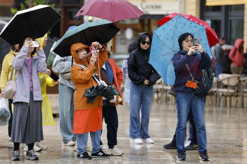 Un grupo de turistas se protege de la lluvia con paraguas este lunes en València. EFE/Ana Escobar
