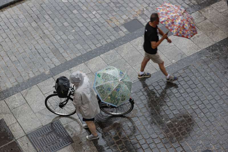 Dos personas caminan bajo la lluvia en una calle de Valencia este sábado. EFE/Manuel Bruque