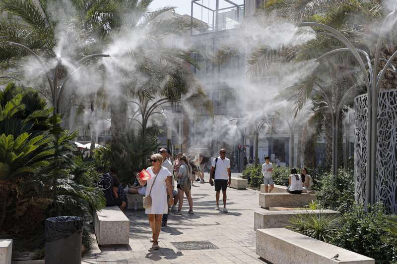 Imagen de archivo de varias personas paseando por el centro de Valéncia, mientras tratan de mitigar el calor bajo la fuente que pulveriza agua en la plaza de la Reina. / EFE-Manuel Bruque