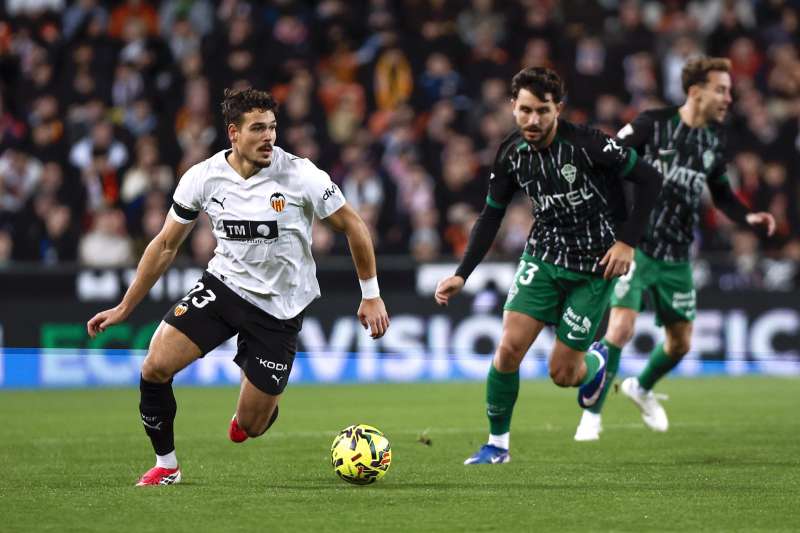 El centrocampista suizo del Valencia Filip Ugrini? (i) dirige el balón durante el partido de la jornada 19 de LaLiga EA Sports que disputan el Valencia CFy el Elche CF este sábado, en el estadio de Mestalla. EFE/ Biel Aliño
