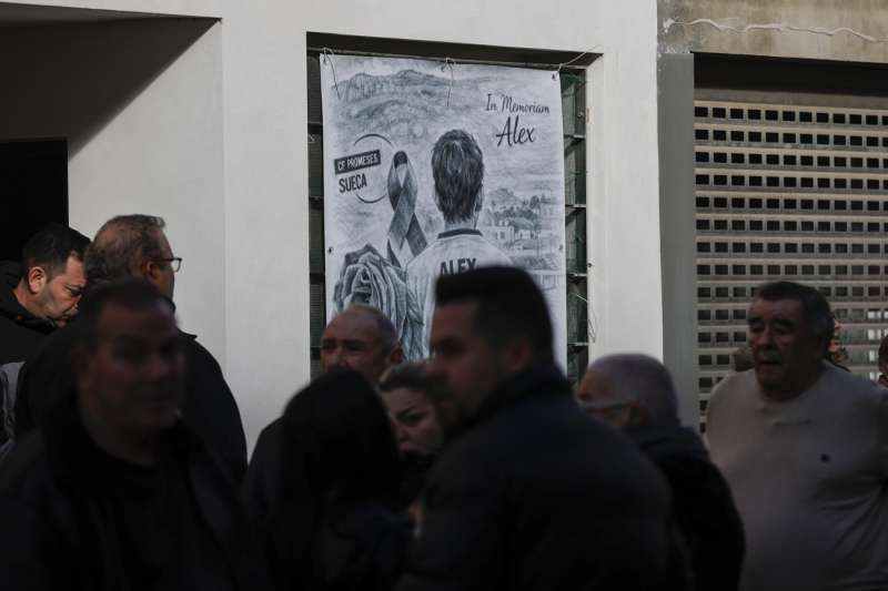 Varias personas aguardan junto a un cartel en memoria de la víctima al pase a disposición judicial del hombre de 48 años que se entregó el pasado sábado en el cuartel de la localidad valenciana de Sueca y confesó haber matado a un menor de 13 años con el que jugaba su hijo en la vivienda familiar. EFE/Manuel Bruque

