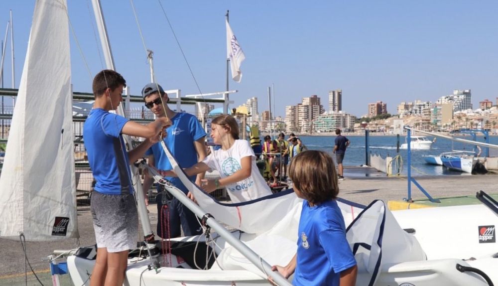 Un grupo de jóvenes prepara su embarcación durante uno de los cursos de verano de la Escuela de Vela del Club Náutico Campello. / Escuela de Vela del Club Náutico Campello Un grupo de jóvenes prepara su embarcación durante uno de los cursos de verano de la Escuela de Vela del Club Náutico Campello. / Escuela de Vela del Club Náutico Campello