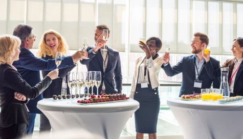 Asistentes brindan durante un evento tipo cóctel con mesas altas, bebidas y aperitivos.